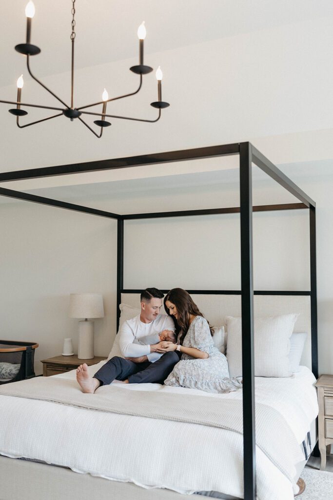 husband and wife sitting on bed with newborn