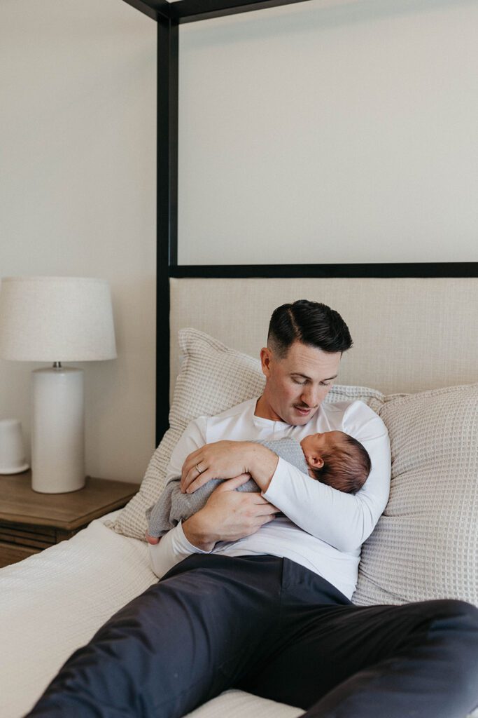 husband holding newborn baby on bed