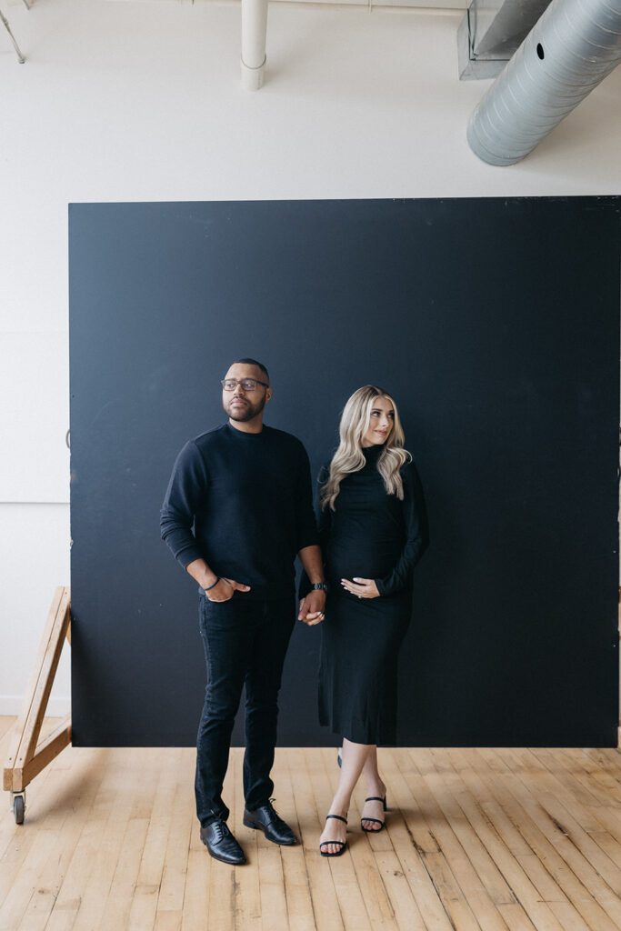 couple posing in front of backdrop for maternity photos