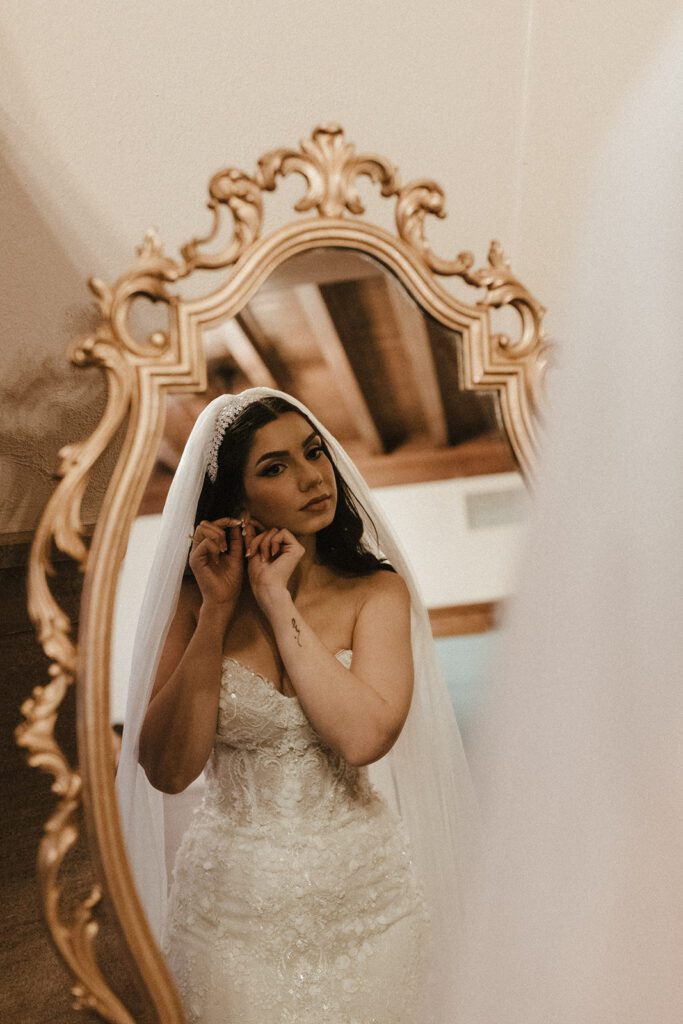 bride getting ready and putting on jewelry in mirror before ceremony